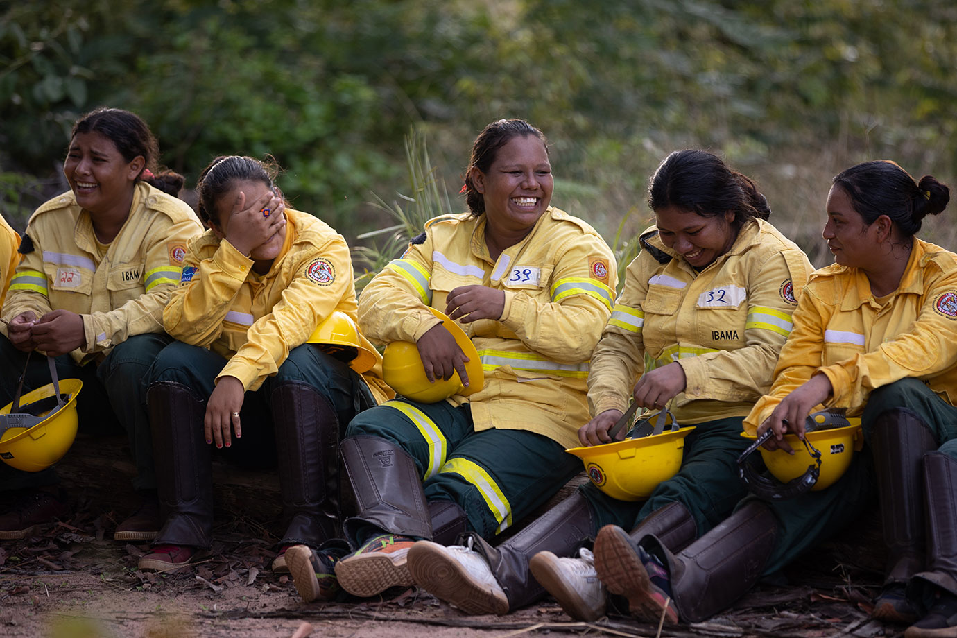 Mulheres indígenas da brigada contra incêndios, sentadas, em área de campo queimado.